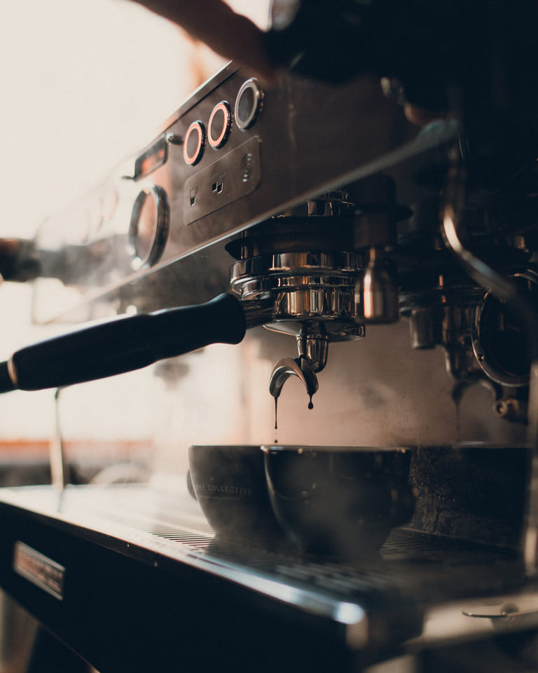 Gros plan artistique d'une machine à café professionnelle en pleine extraction, laissant couler de fines gouttes d'espresso dans une tasse sombre.