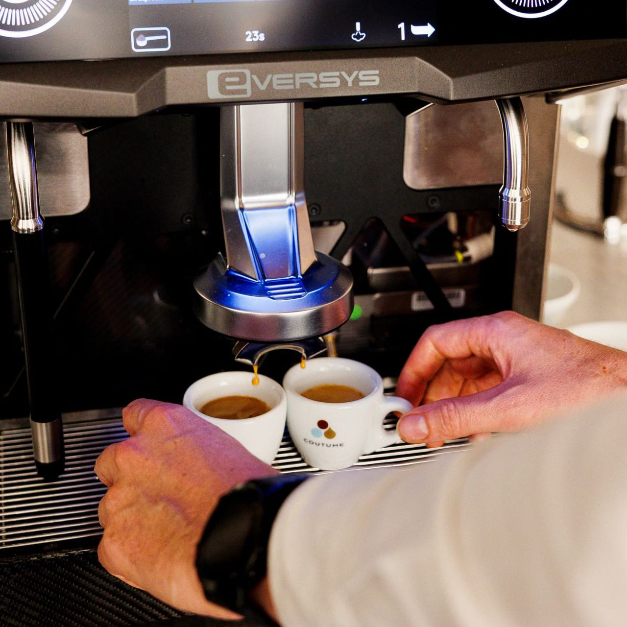Vue de profil d'une machine à café automatique au design épuré, mise en valeur par un éclairage doux sur un comptoir sombre.